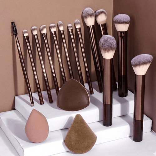 Set of makeup brushes and beauty sponges on a white platform with a brown background